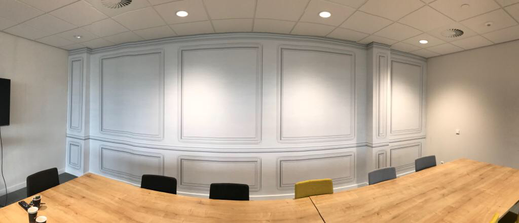 Vergaderruimte met een lange tafel en een wand met klassieke panelen